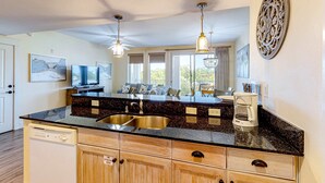 A modern kitchen with granite countertops, stainless steel sink, wooden cabinets, and pendant lighting. - Delightful condo with pools, hot tub, tennis court, grilling area (Miramar Beach)