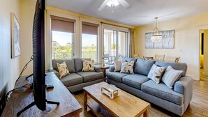 A living room with a gray sofa, a wooden coffee table, a TV on a stand, and a ceiling fan. - Delightful condo with pools, hot tub, tennis court, grilling area (Miramar Beach)