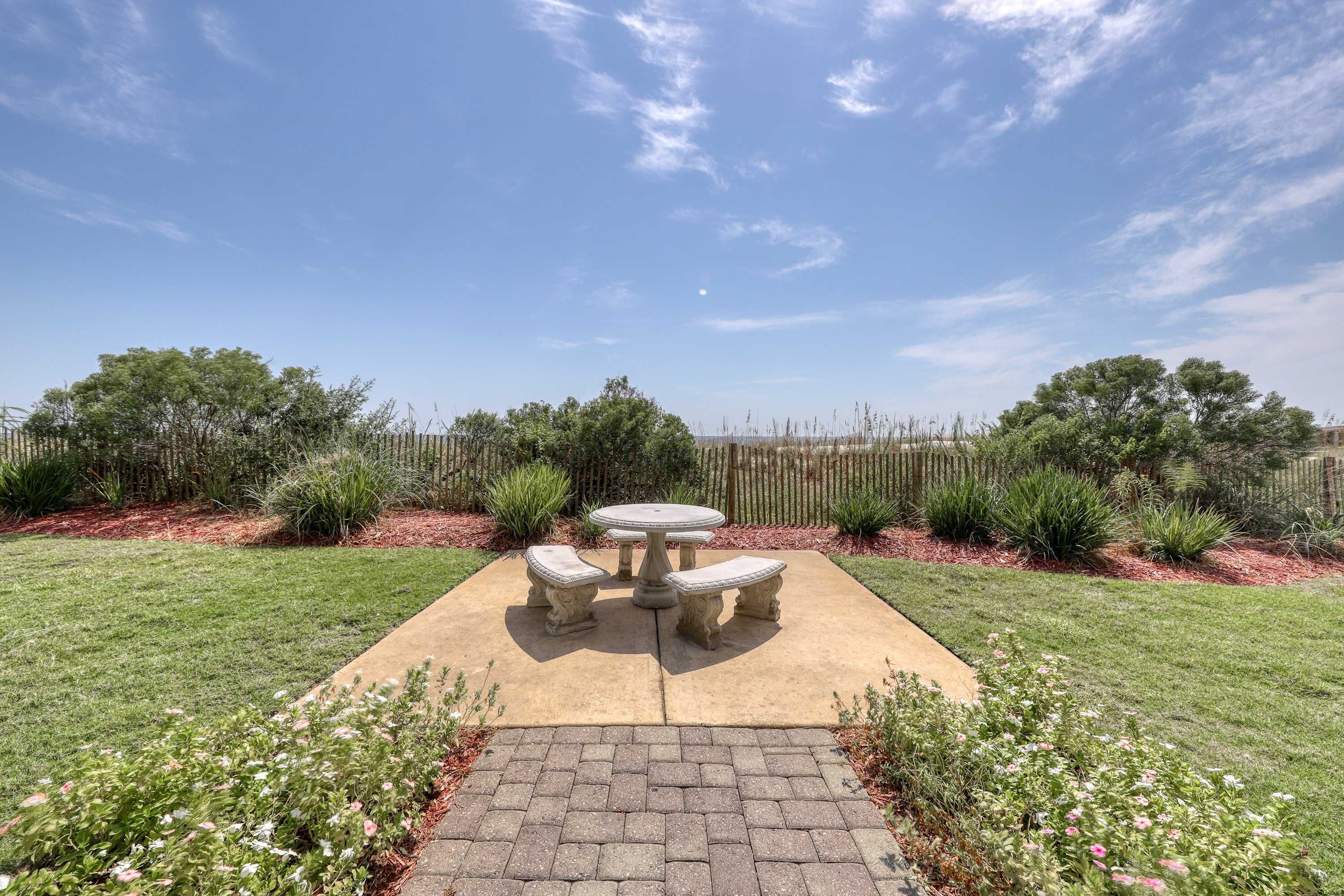 A patio with a stone table and four chairs, surrounded by a well-maintained lawn and various plants.