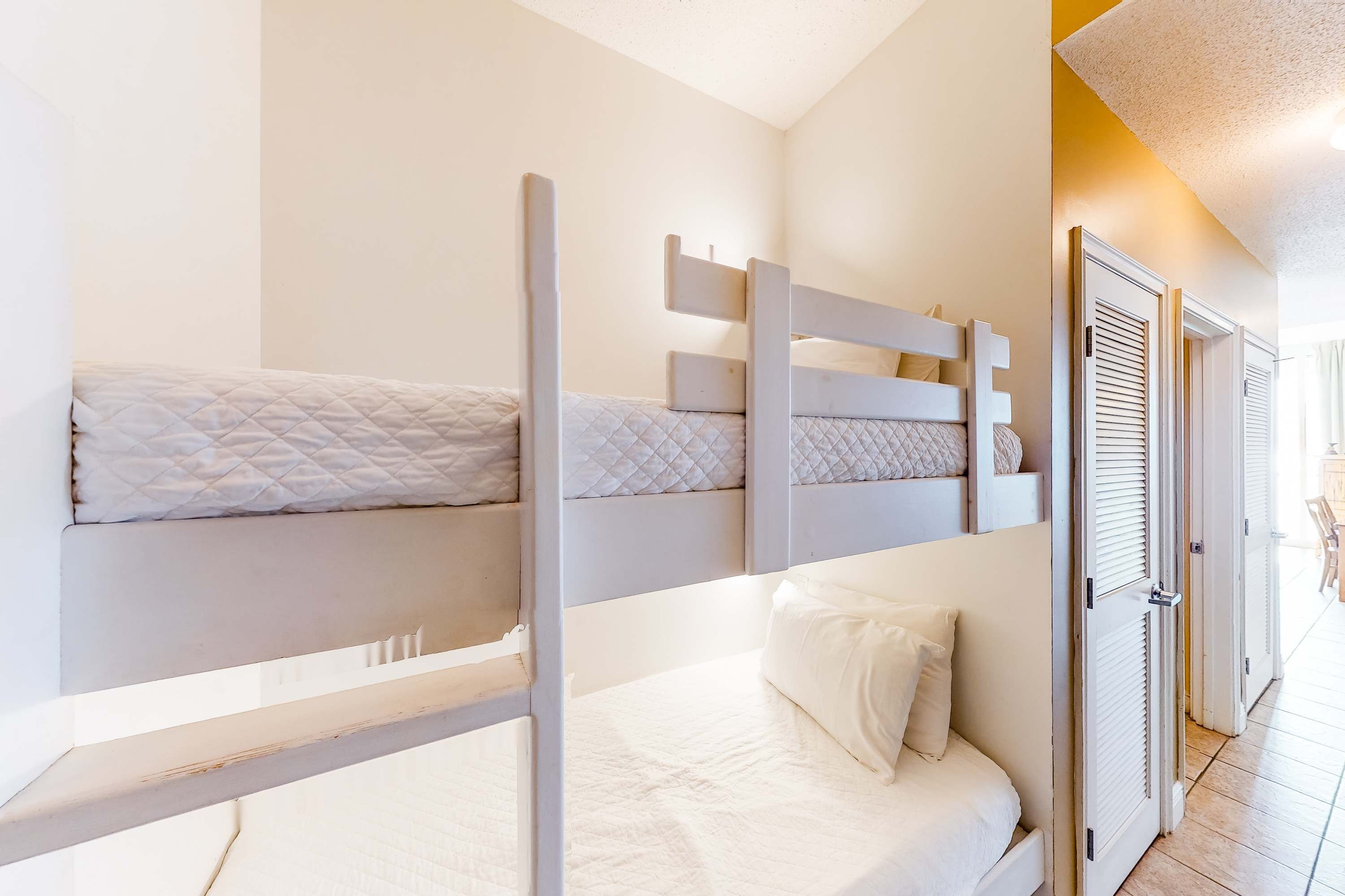 Habitación con literas, ropa de cama blanca y una puerta que da a un pasillo.