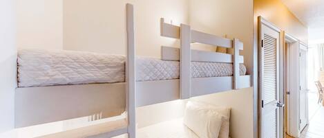 Habitación con literas, ropa de cama blanca y una puerta que da a un pasillo.