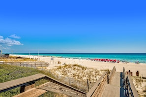 Une plage avec une promenade en bois menant au rivage, un ciel bleu clair et une eau turquoise.