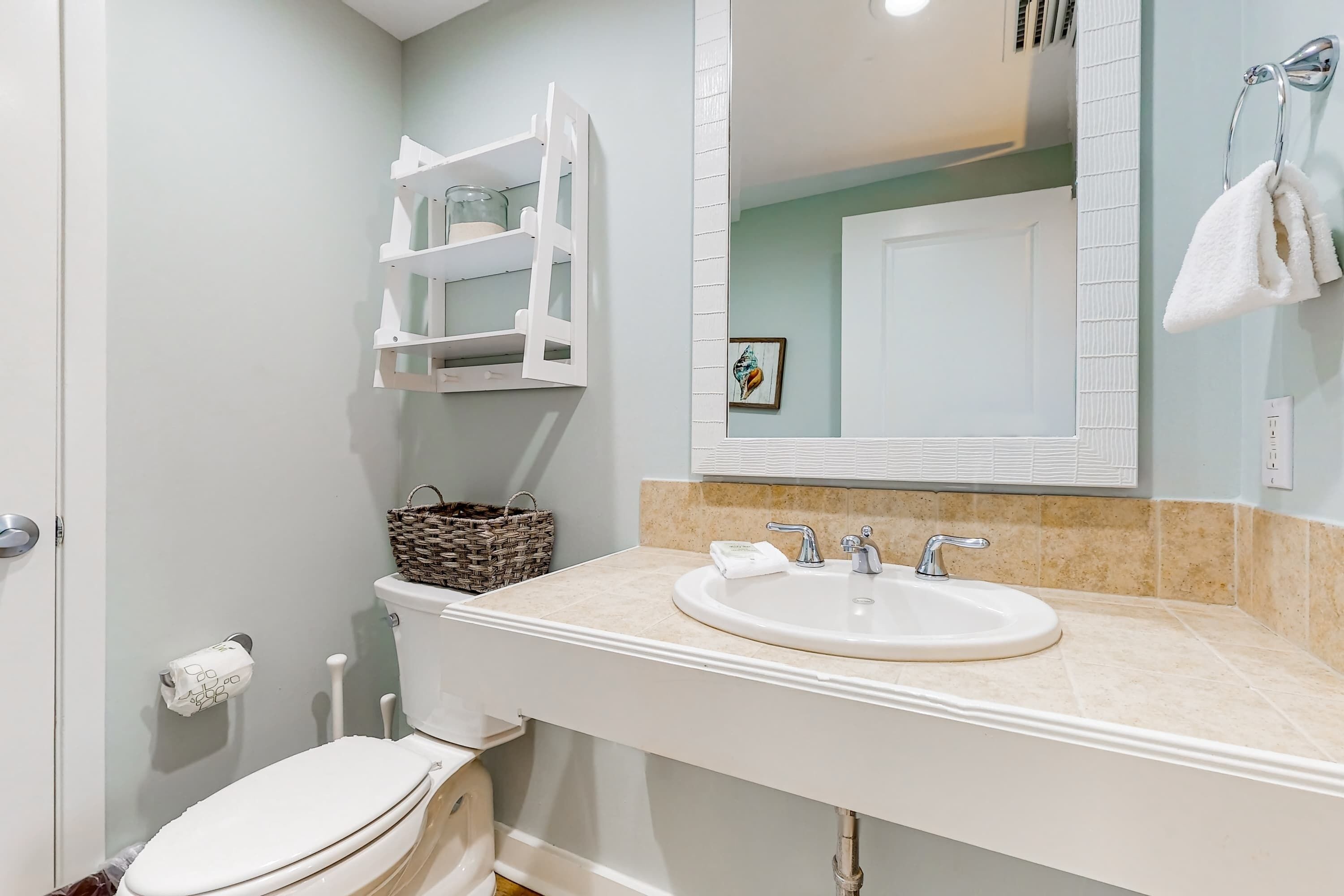 Un baño con inodoro, lavamanos y estante blanco.