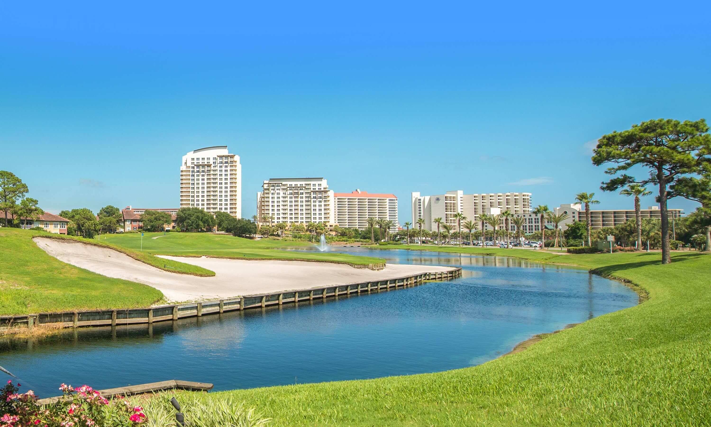 Campo de golf con un estanque, rodeado de edificios y vegetación.