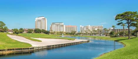 Campo de golf con un estanque, rodeado de edificios y vegetación.