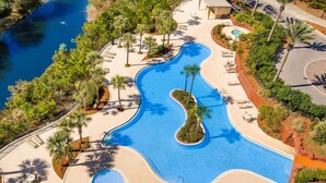 Una piscina ampla i sinuosa envoltada de palmeres i gandules, amb vista a un riu.
