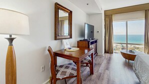 Habitació d'hotel amb taula de menjador de fusta, cadires, televisió i vista a l'oceà.