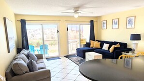 Sala de estar con sofá, mesa de comedor, ventilador de techo y puerta corrediza de vidrio que da a un área exterior.