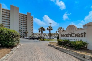 Une enseigne indiquant l’emplacement des appartements BeachCrest, avec une entrée dallée, des voitures garées et de grands immeubles en arrière-plan.