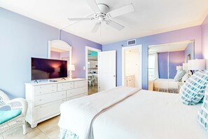 Une chambre à coucher avec un lit, une télévision, une commode, un ventilateur de plafond et une porte menant à la salle de bain.