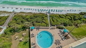 An aerial view of a beach resort with a swimming pool surrounded by lounge chairs and umbrellas, a deck leading to the beach, and a well-maintained garden area. - Beach front condo with washer&dryer, shared pool and beach access (Santa Rosa Beach)