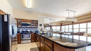 Una cocina moderna con una isla grande, electrodomésticos de acero inoxidable, armarios de madera y un ventanal que proporciona luz natural.