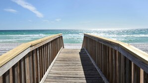 Un muelle de madera que lleva a una playa bajo un cielo azul despejado.