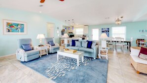 A spacious living room with a ceiling fan, a coffee table, two sofas, and a dining area with a table and chairs. - Beachside home with private pool & amazing views (St. George Island)