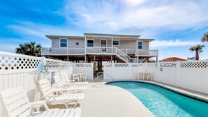 A pool area with white lounge chairs, a pool, and a two-story building with a balcony. - Beachside home with private pool & amazing views (St. George Island)