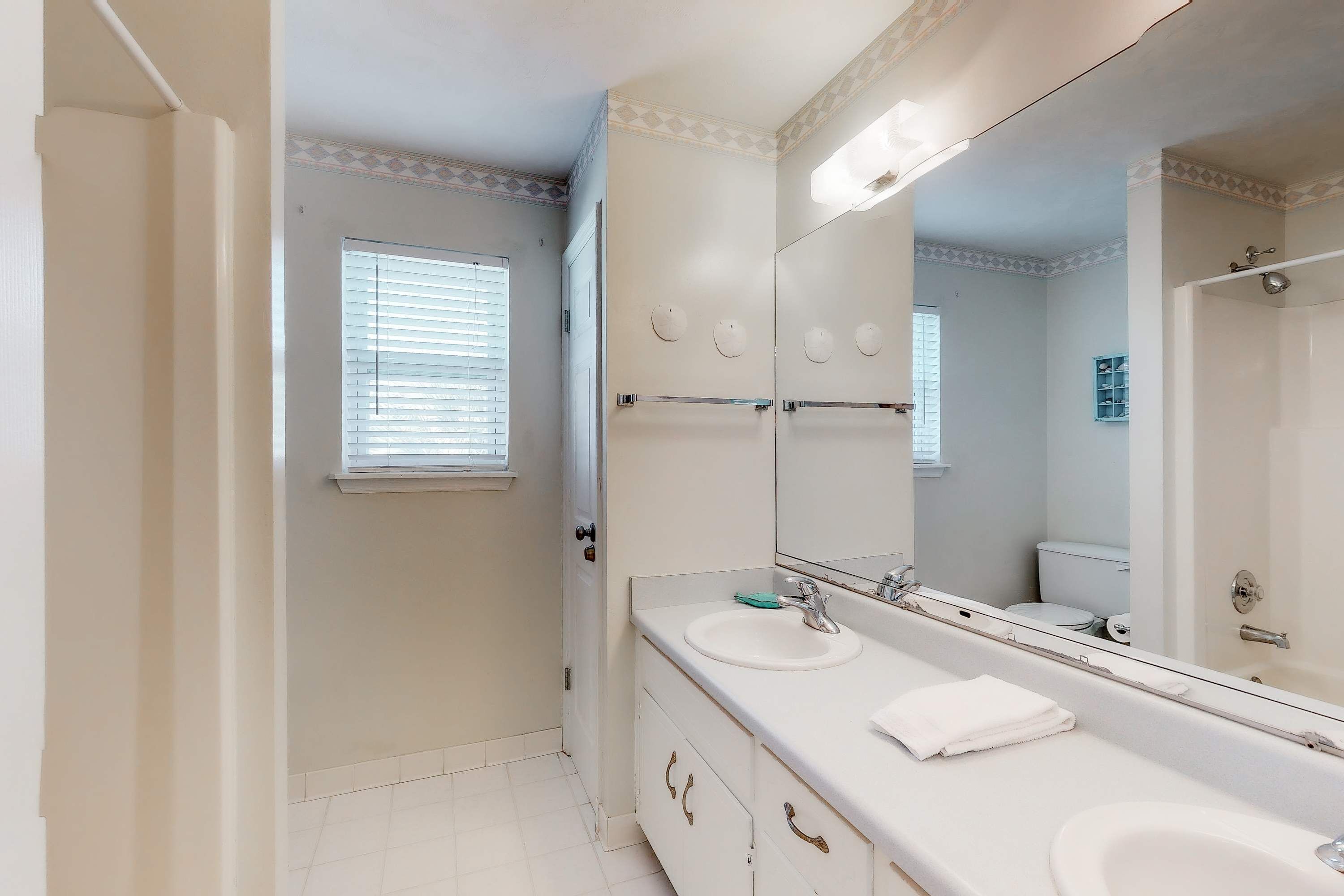 A bathroom with two sinks, a large mirror, and a window with blinds.