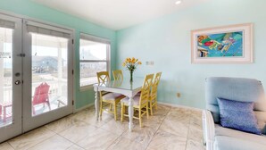 A dining area with a table and chairs, a blue wall, a framed picture, and a view through a glass door. - Beachside home with private pool & amazing views (St. George Island)