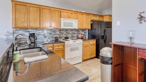 A kitchen with wooden cabinets, a stainless steel sink, a microwave, a stove, and a refrigerator. - Dog-friendly coastal home with a game room and covered patio (Port St. Joe)