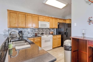 A kitchen with wooden cabinets, a stainless steel sink, a microwave, a stove, and a refrigerator. - Dog-friendly coastal home w/ a game room and covered patio (Port St. Joe)