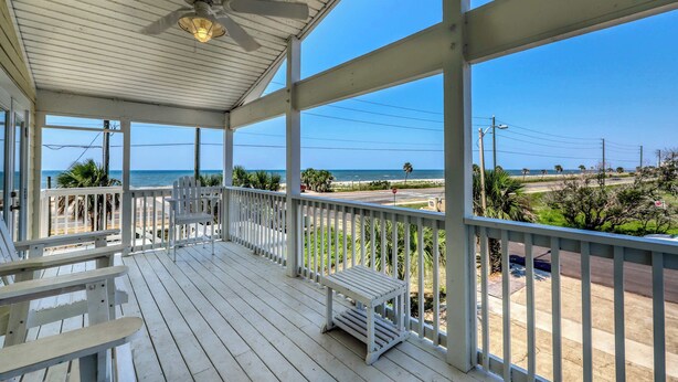 A covered porch with white railings and a ceiling fan, overlooking a beach and road. - Dog-friendly coastal home with a game room and covered patio (Port St. Joe)
