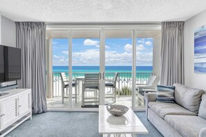 A modern hotel room with a balcony overlooking a beach, a flat-screen TV, a sofa, and a coffee table. - Seaside condo with wonderful beach views, balcony, grill, pool, hot tub, & gym (Fort Walton Beach)