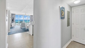 A hallway leading to a room with a view of the ocean, a white door, and a framed picture on the wall. - Seaside condo with wonderful beach views, balcony, grill, pool, hot tub, & gym (Fort Walton Beach)