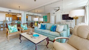 A spacious living room with a sofa, chairs, a coffee table, and a television. - Pretty Gulf Front Condo Fun Amenities, Nearby Shopping & Dining! (Fort Walton Beach)