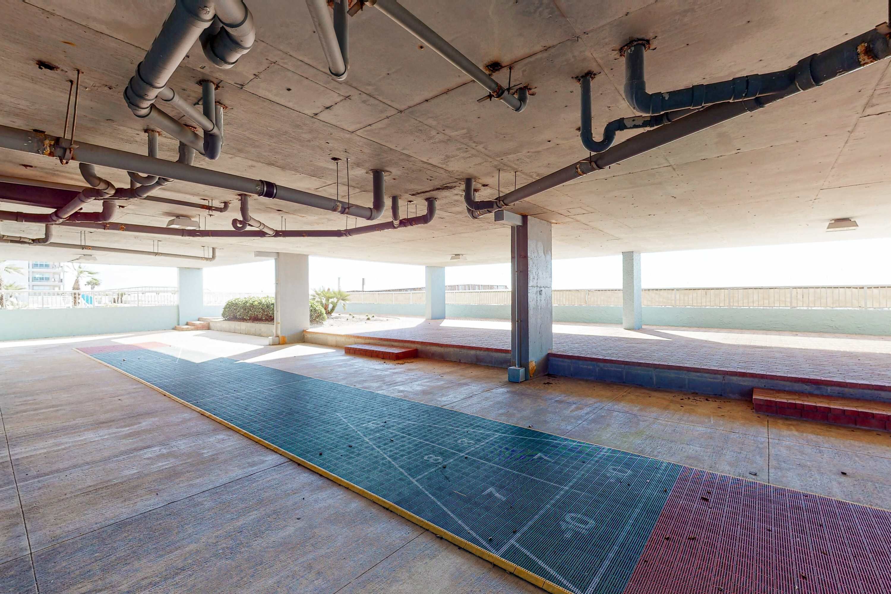 Un parking souterrain vide, avec des piliers en béton, des tuyaux apparents et un chemin en pavé tactile bleu.