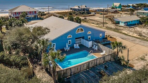 A large blue house with a swimming pool, surrounded by a wooden fence and palm trees.