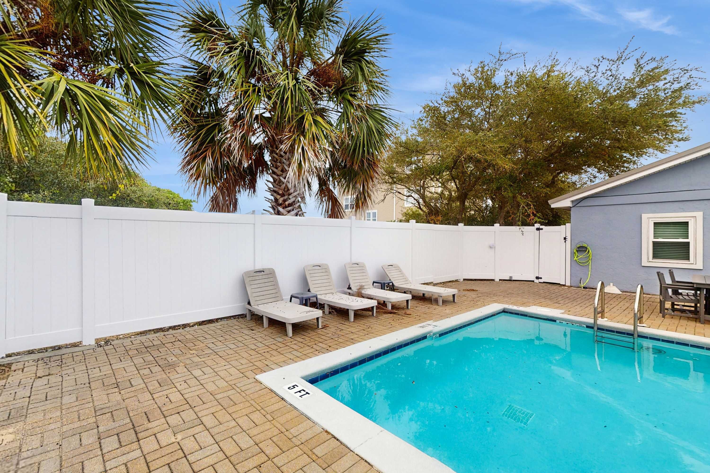 A swimming pool with lounge chairs, a white fence, and palm trees.