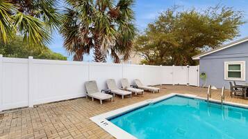 A swimming pool with lounge chairs, a white fence, and palm trees.