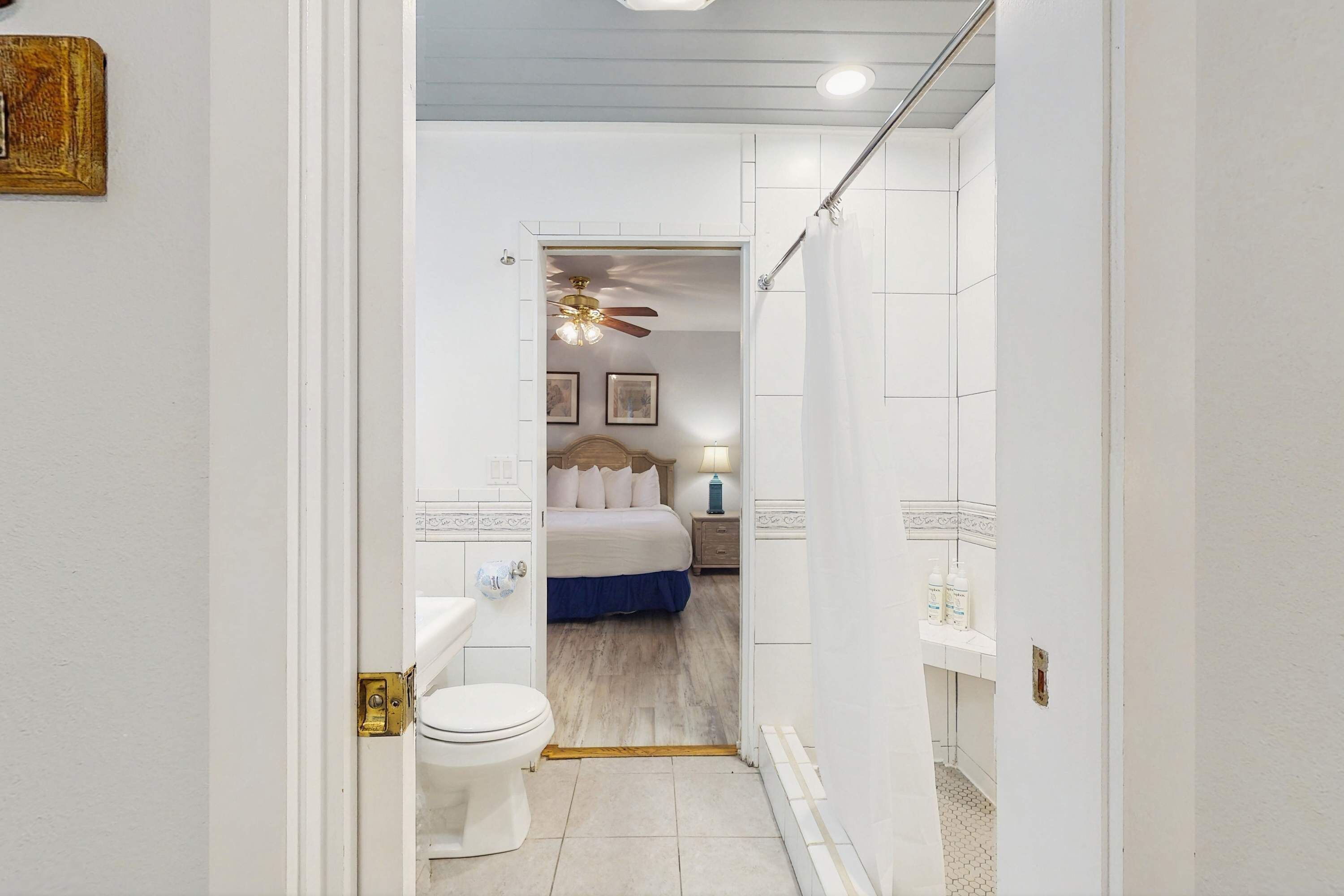 Ein schmaler Flur, der in ein Schlafzimmer mit Bett, Nachttisch und Deckenventilator führt.