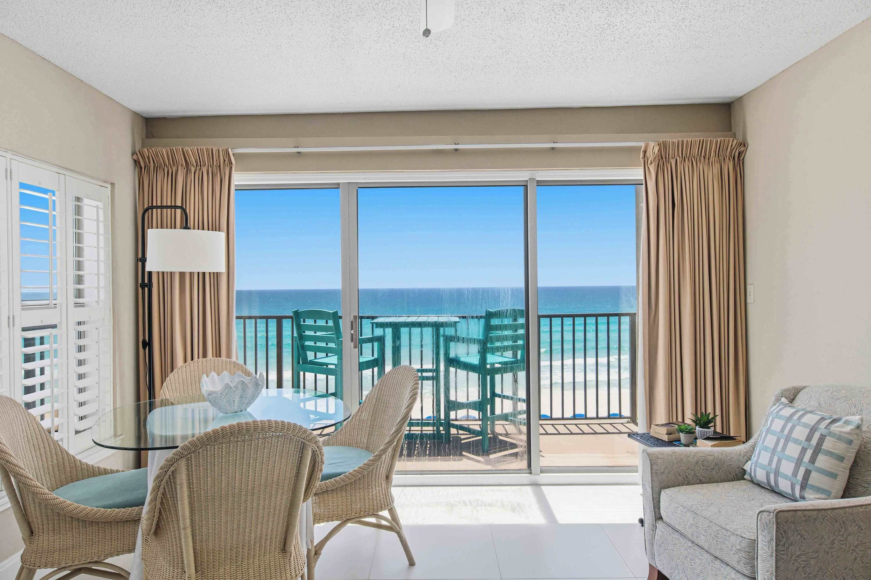 A balcony with a view of the ocean, wicker furniture, and a glass table.