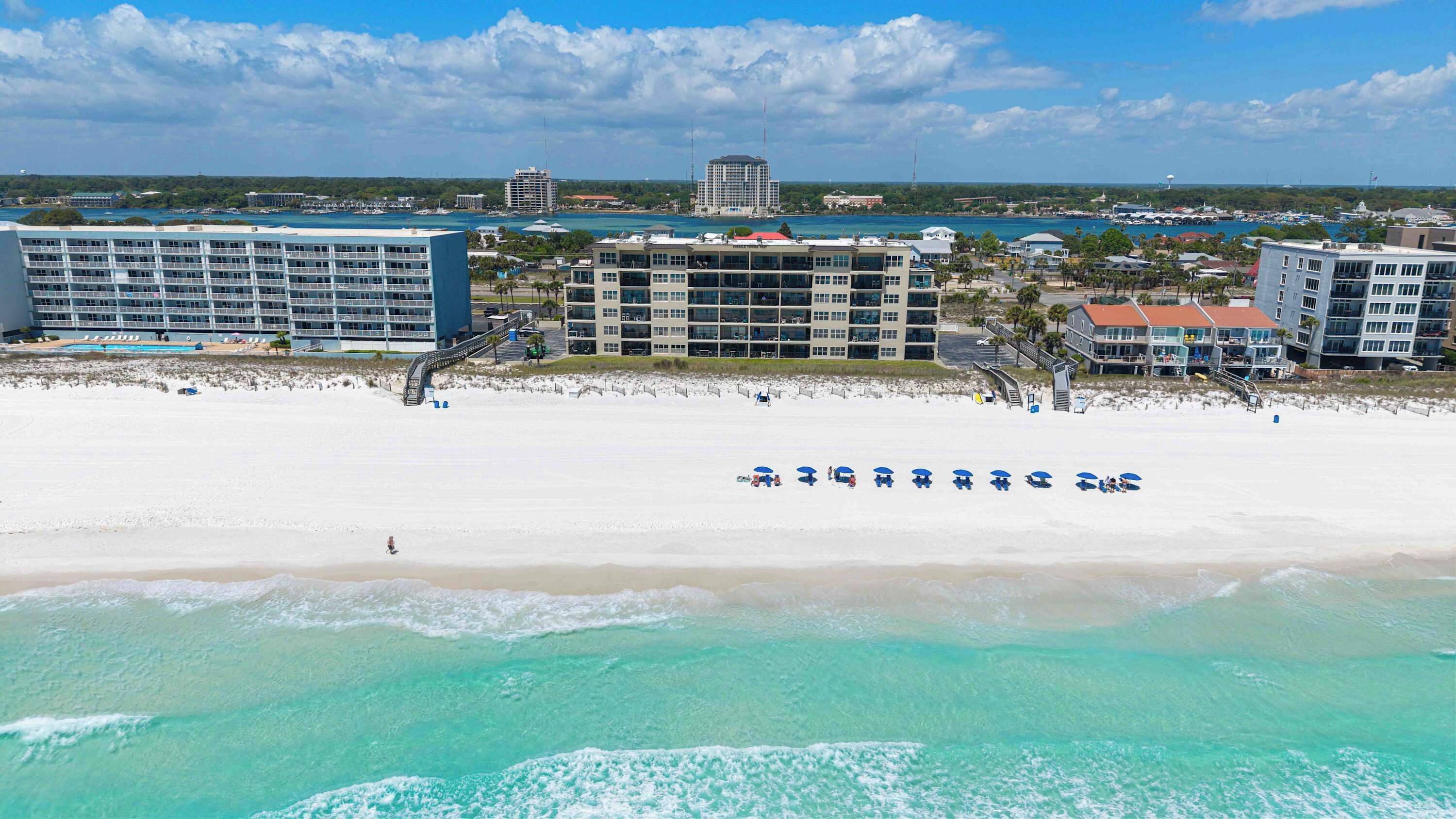 A beach resort with multiple-story buildings, a sandy beach, and a clear view of the ocean.