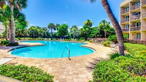 Una piscina circondata da palme e lettini, con un edificio sullo sfondo.