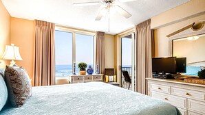 Ein Hotelzimmer mit einem großen Bett, einem Fernseher, einem Schminktisch und Blick aufs Meer.