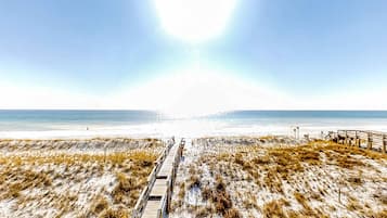 Een strand met een houten looppad naar het water, zandduinen en een heldere lucht.