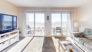 Uma sala de estar com televisão, sofá, mesa de centro e varanda com mobiliário exterior.