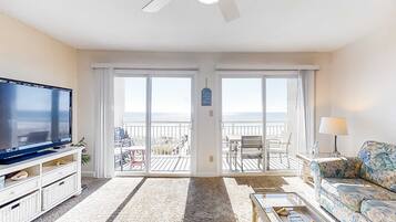 A living room with a television, a sofa, a coffee table, and a balcony with outdoor furniture.