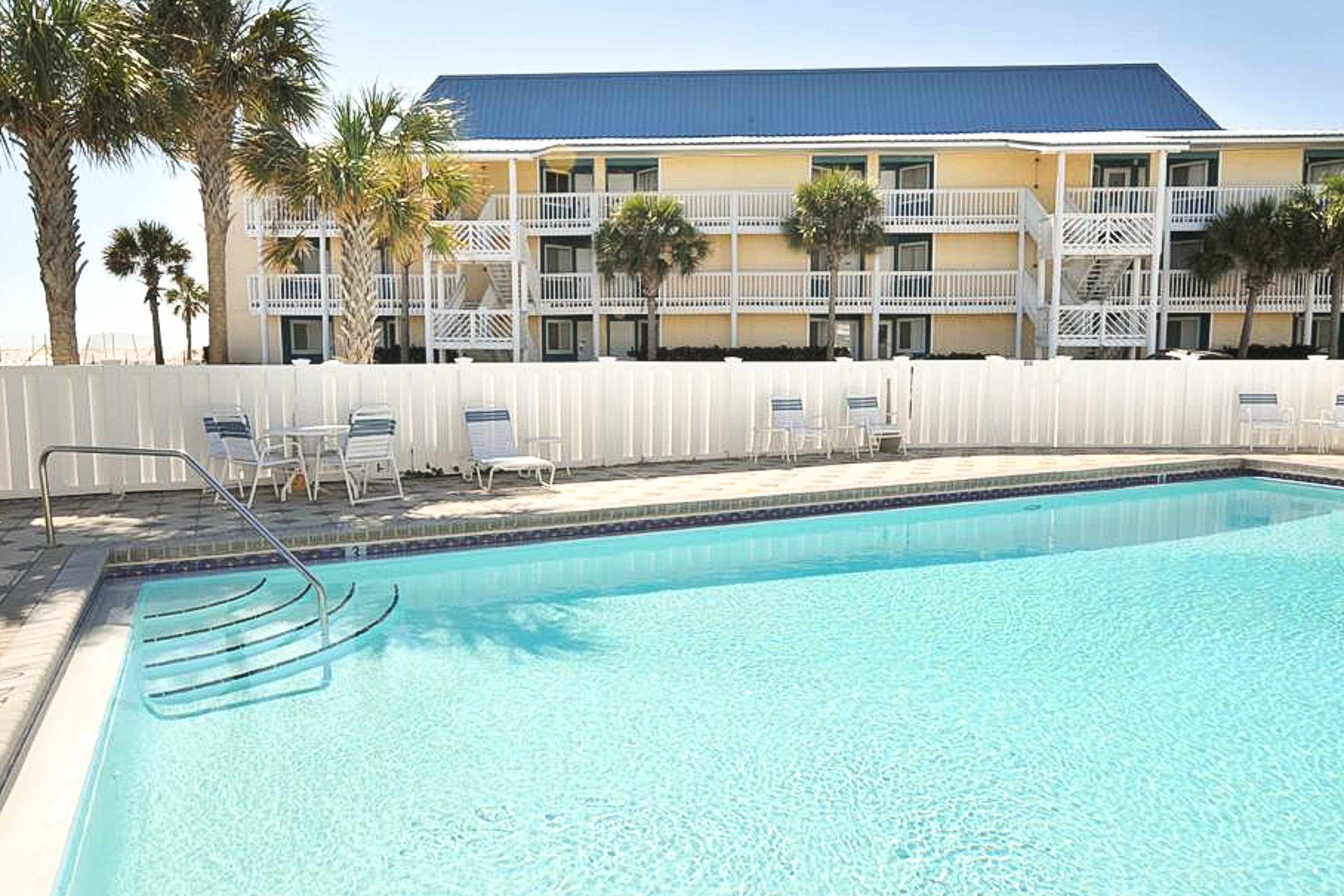 A swimming pool with lounge chairs and a white fence.