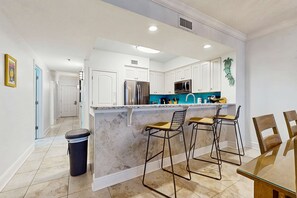 A modern kitchen with white cabinets, a marble island, and bar stools. - Modern , Beachfront Condo with Shared Pools, Nearby Activities, Shops, Restaurants (Fort Walton Beach)