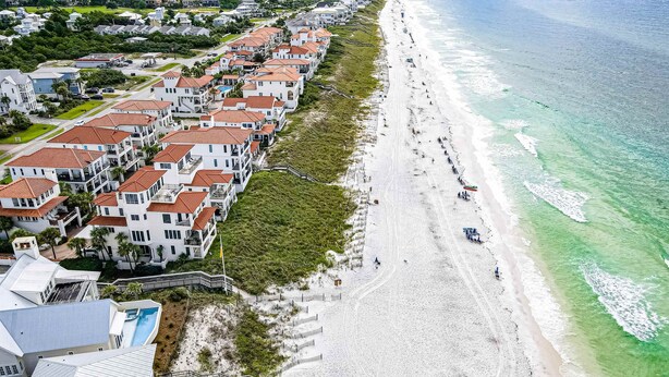 Una zona residencial frente al mar, con propiedades en primera línea de playa, una playa de arena y una vista despejada del océano.