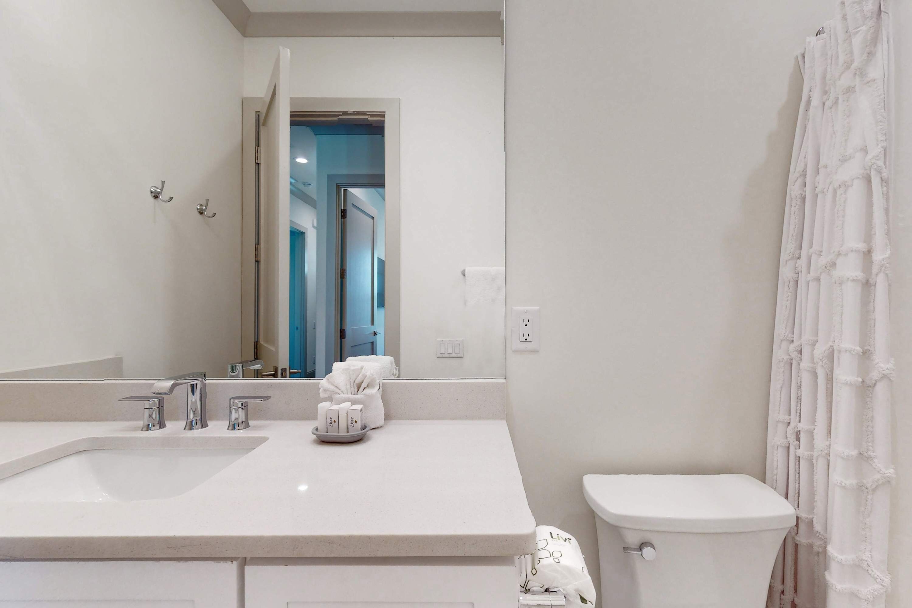 A modern bathroom with a white sink, two faucets, a toilet, and a shower curtain.