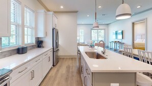 Una cocina moderna con armarios blancos, una isla grande con un lavamanos y un comedor con sillas blancas.