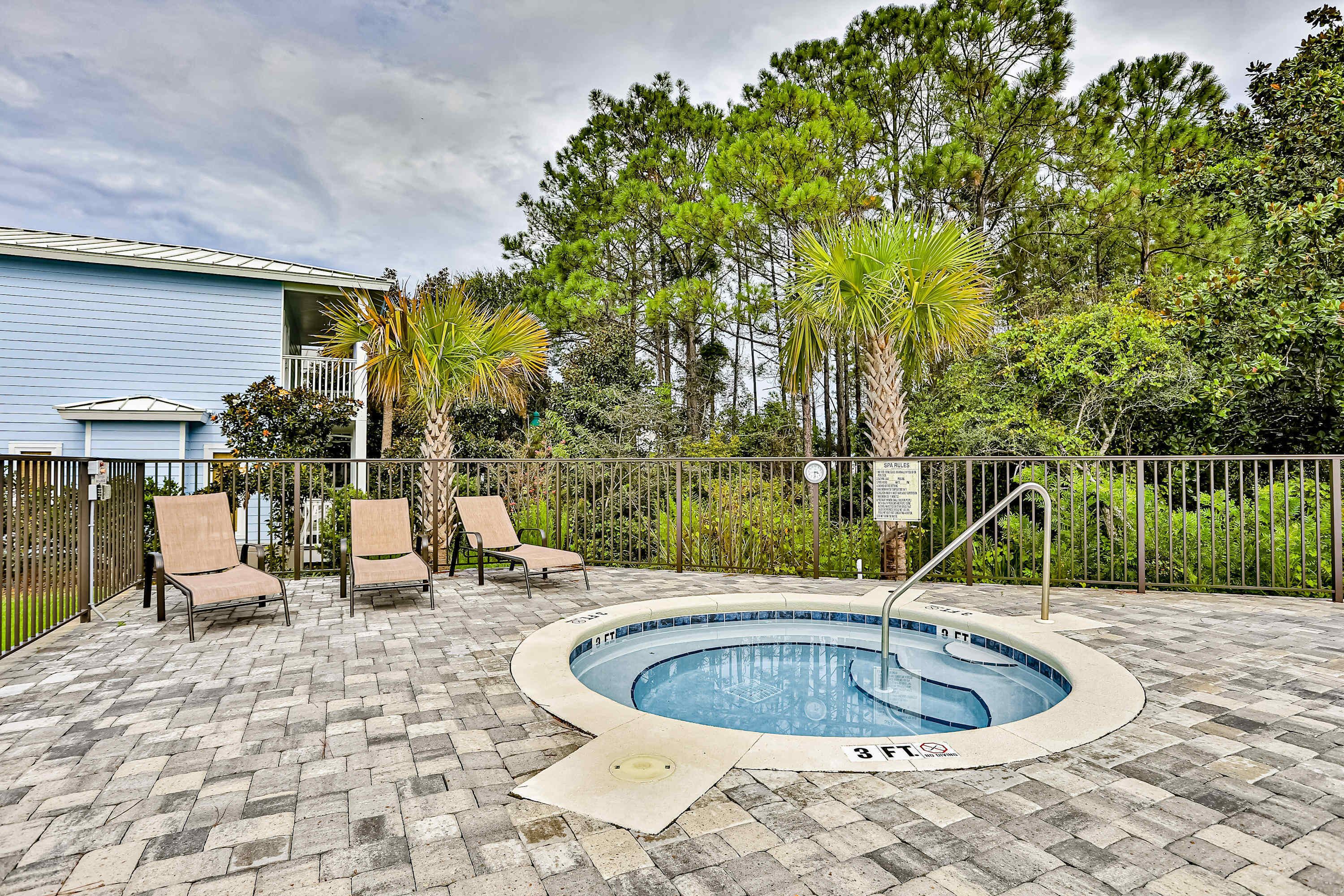 A pool area with a hot tub, lounge chairs, and a fenced patio.