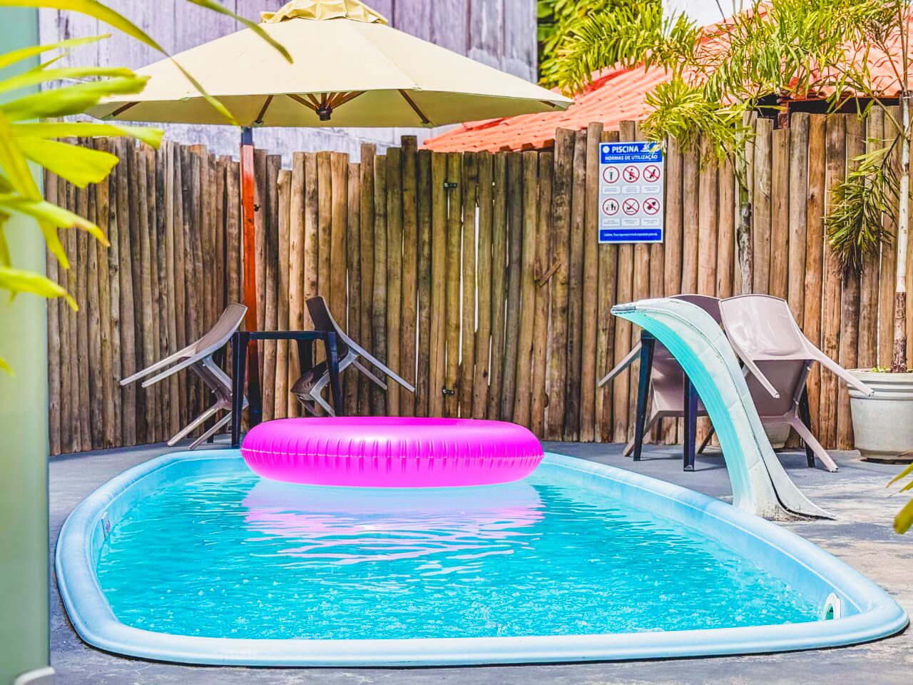 A swimming pool with a pink inflatable ring, a wooden fence, and lounge chairs.