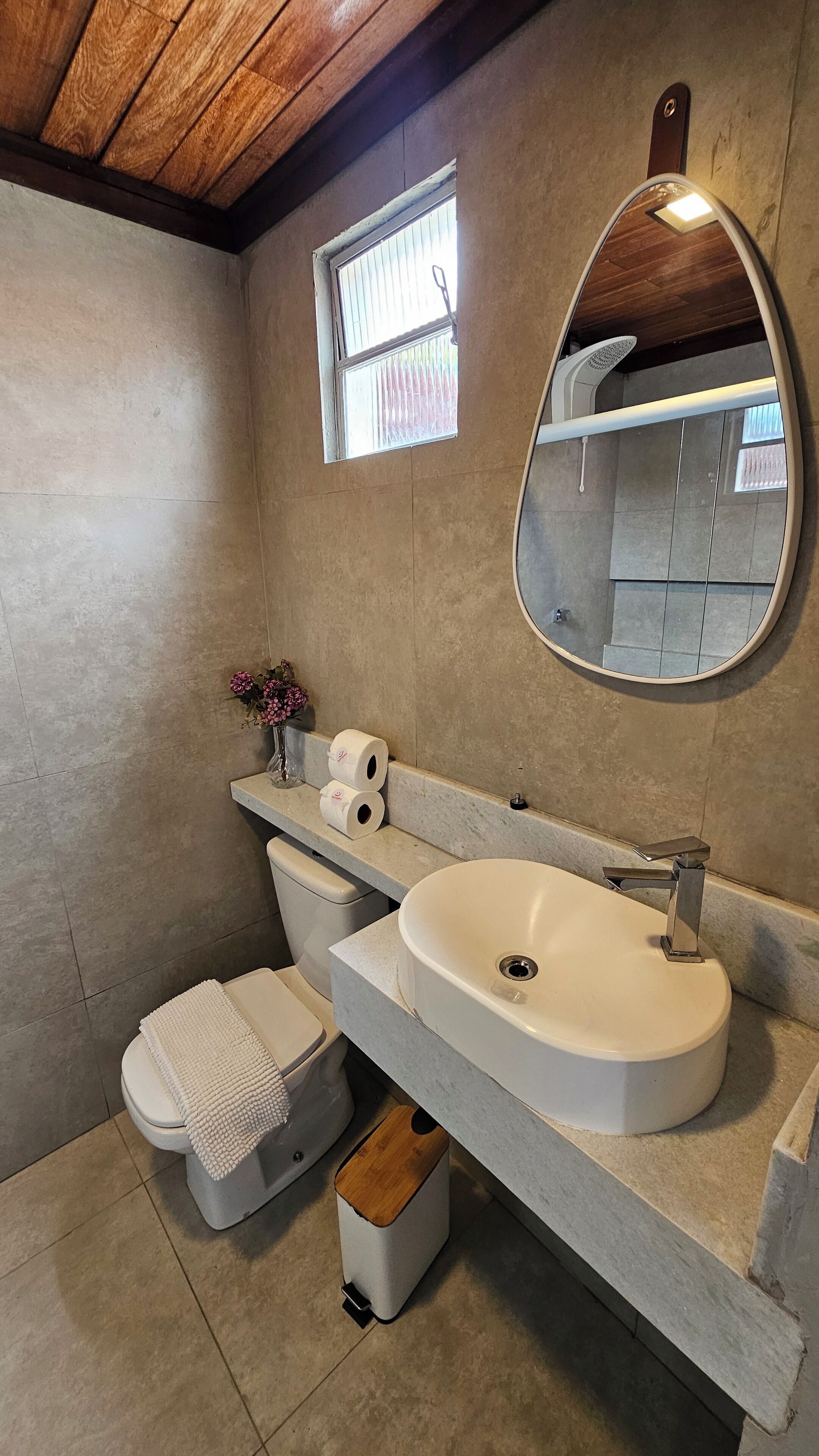Un bagno moderno con uno specchio ovale grande, un lavandino bianco e un water.