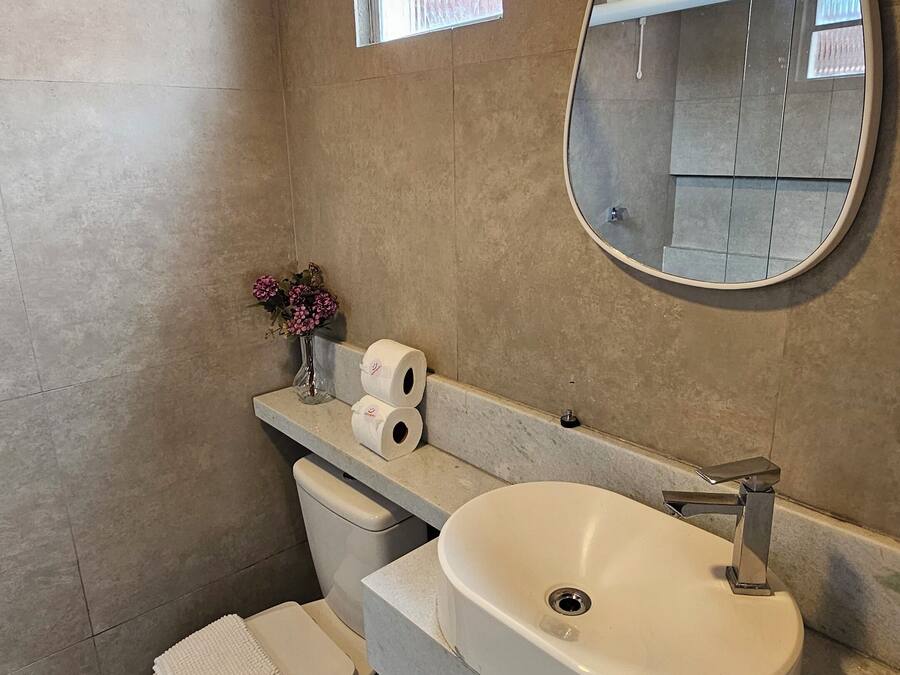 A modern bathroom with a large oval mirror, a white sink, and a toilet.