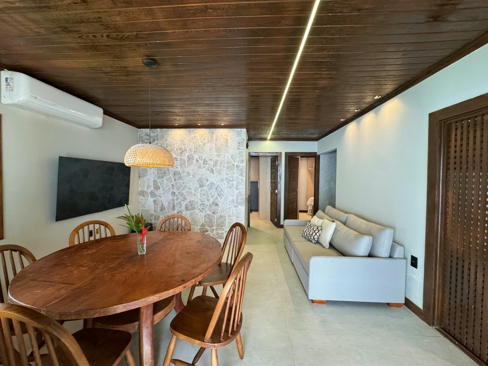 Uma sala de jantar com mesa e cadeiras de madeira, parede decorativa de pedra e design moderno no teto.