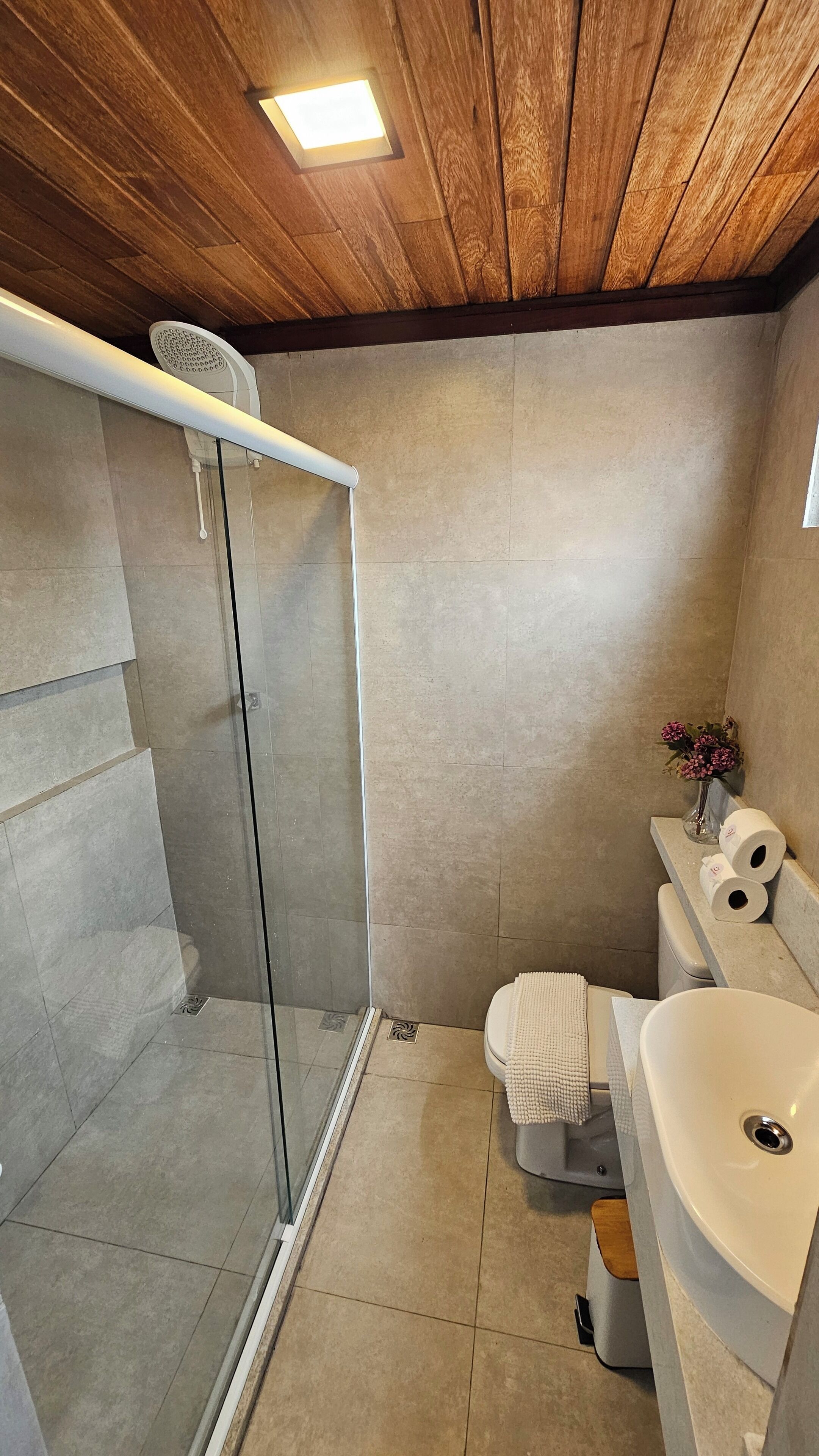 Un baño con ducha de vidrio, inodoro y lavamanos con un jarrón de flores.
